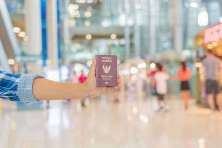 Hand holding Thai passport at the airport with beautiful bokeh background,traveler concept.の写真素材