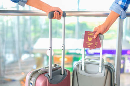 Man's hand hold Passport,Man & Woman hold  luggage, at the airport ,thailand passport The text on that cover means "Thailand passport",traveler concept.の写真素材