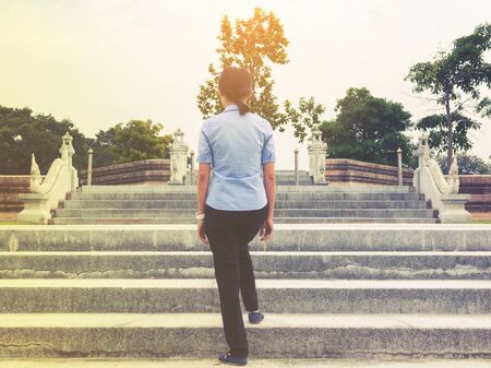 back view of young business woman walking to top of stairs, attempt to target concept