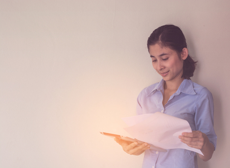 young asian woman standing and holding worksheet and tablet over gray backgroundの写真素材