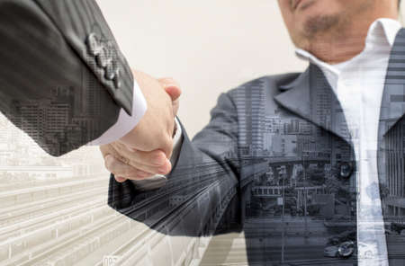 Businessmen shaking hands making an agreement, Double exposure of handshake and cityの写真素材