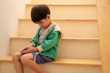 A boy who was scolded by his mother secretly came to play on the phone on the stairs.の写真素材