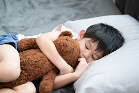 A boy is sleeping and hugging a teddy bear in bed.の写真素材