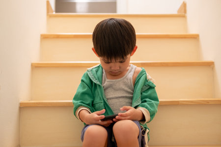 A boy who was scolded by his mother secretly came to play on the phone on the stairs.の写真素材