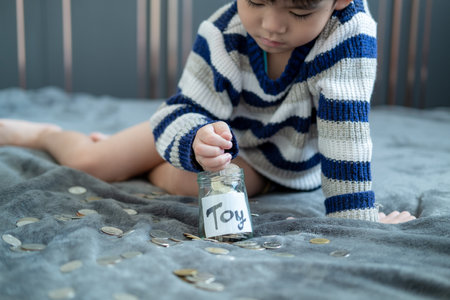 Asian boy sits and puts coins in a glass jar to save money to buy toys.の写真素材