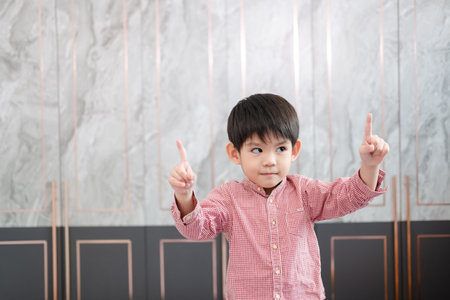 An Asian boy stands and smiles, raising both hands and pointing upwards.の写真素材