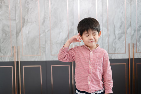 Asian boy stands with his hand pointing at his head. Pretending to be thinking about somethingの写真素材