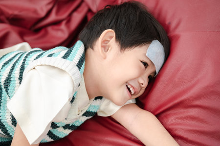 Asian boy Lying sick with a fever reducing patch on her forehead but still smiling.の写真素材