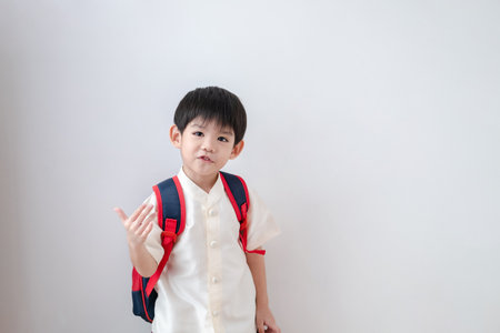 Asian boy Wearing traditional Thai clothing, standing with a school bag. Make a beckoning gesture preparing to go to school on a white backgroundの写真素材