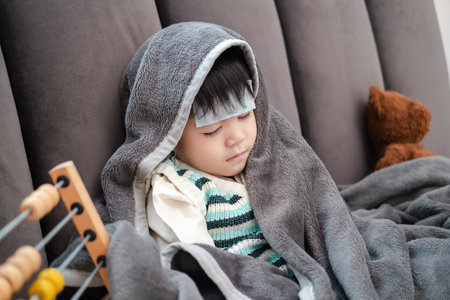 Asian boy Lying sick, he had a fever reducing patch on his forehead and covered himself with a blanket because of the cold.の写真素材