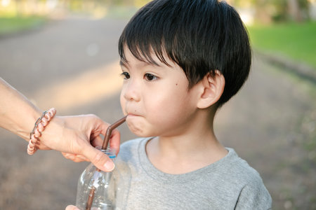 Asian boy drinking water from a bottle held by his motherの写真素材