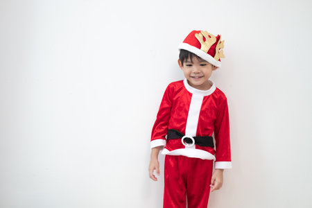 Asian boy wearing Santa costume Standing and playing near A fun Christmas tree on white background.の写真素材
