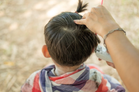 Barber cutting hair of an Asian boy In an open space filled with trees.