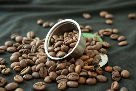 Coffee beans inside and around a refillable coffee capsule on a black background.の写真素材