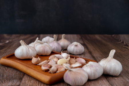 A large head of garlic lies on a wooden plate on a black background.の写真素材