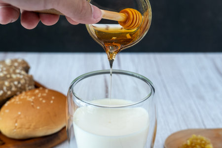 Breakfast set Male hand pouring honey into a glass of milk with breadの写真素材