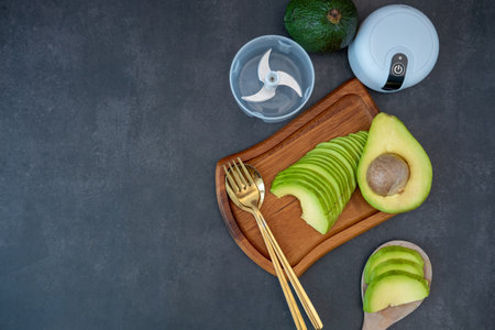 Top view of halved and finely sliced avocado on wooden plate on black background.