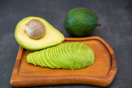 Top view of halved and finely sliced avocado on wooden plate on black background.の写真素材