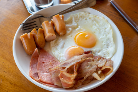 Breakfast with fried eggs, sausage, bacon is on the table.の写真素材