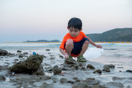 Little Asian boy helps pick up trash on the sea beach.