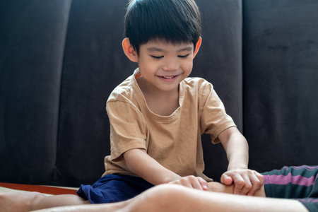 A young Asian child is taking care of his mother by massaging her muscles to relax her.の写真素材