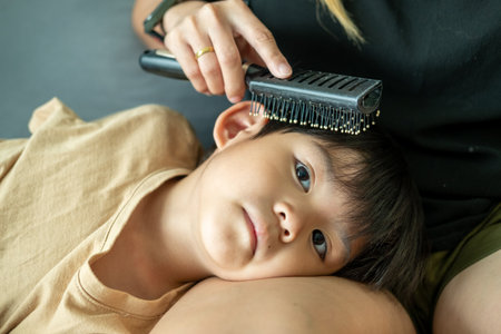 Asian boy lies on his mother's lap, using a comb to comb his hair.
