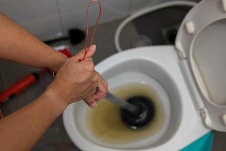A woman's hand is using a plunger to solve a clogged toilet.の写真素材