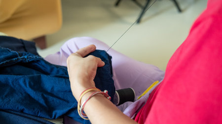 Close-up of a motherâ€™s hands sewing trouser legs, showing family care through homemade...