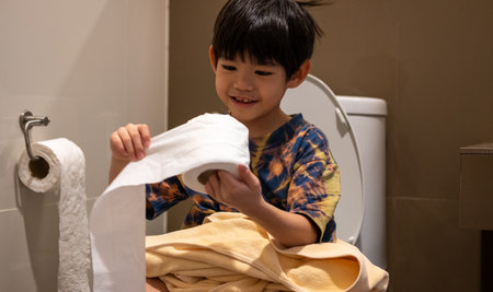 Young Asian boy using toilet with tissue showing personal hygiene and home bathroom settingの写真素材