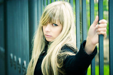 Young woman holding on fence. Soft yellow and blue tinting.の写真素材