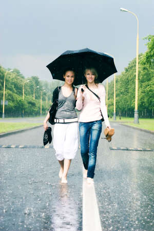 Two women in a heavy rain. Walking on a road.の写真素材