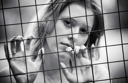 Young woman pensive portrait. Behind the metallic wire.の写真素材
