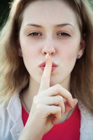 Young woman showing quiet sign. Outdoors portrait.