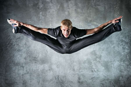 Young man dancer jumping up high. On wall background.の写真素材