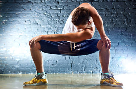 Young man sports exercises. On wall background.