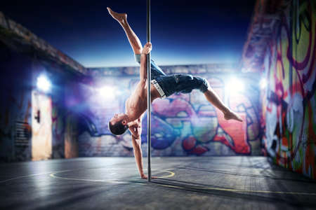 Young strong pole dance man on urban background.