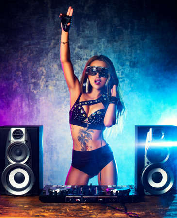 Young sexy woman dj playing music. Big loud speakers, headphones and dj mixer on table.の写真素材