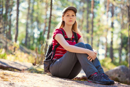 Young woman tourist sitting on stone in summer forest.の写真素材