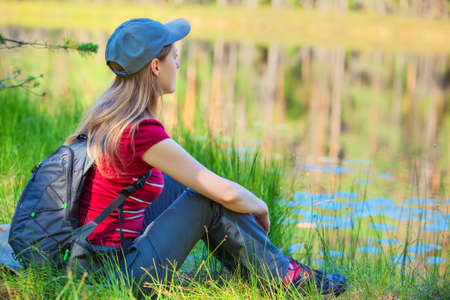 Young woman tourist sitting on grass on pond coast.の写真素材