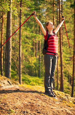 Young woman tourist standing on stone in forest and looking up on sunset.の写真素材