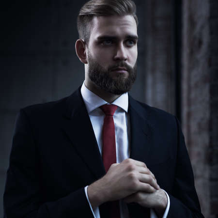 Young serious businessman with beard in black suit portrait.の写真素材
