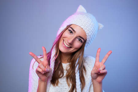 Young happy smiling woman showing victory sign. Warm winter white clothing.