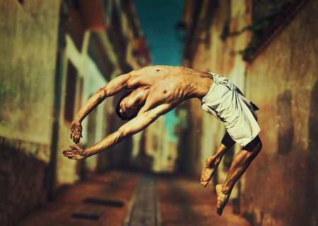 Young man dancer jumping on old town street backgroundの写真素材
