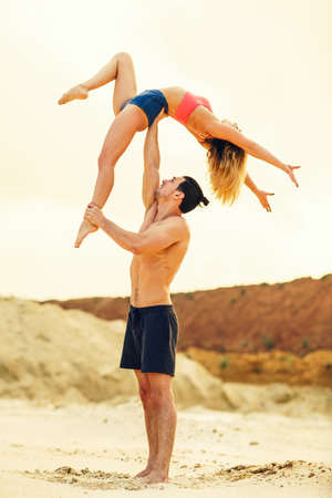 Young sports couple doing acroyoga exercises on sand beachの写真素材
