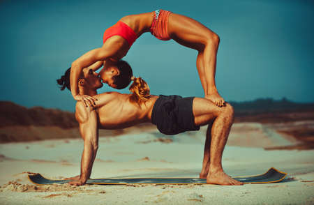 Young sports couple doing acroyoga exercises on sand beach and kissingの写真素材