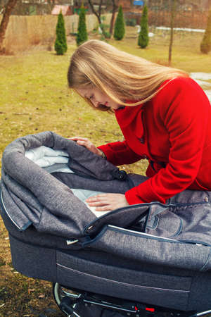Young mother in red coat with baby and carriage at autumn park
