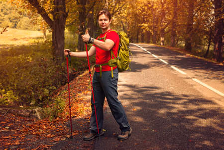 Young man tourist walking with sticks on road and showing thumbs up handsignの写真素材