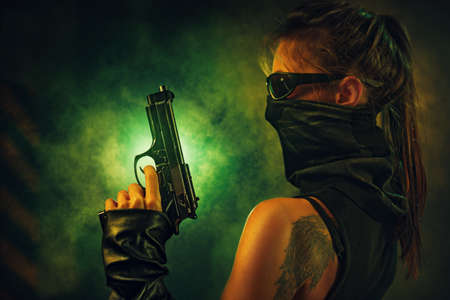 Dangerous woman fighter with gun and scarf in dark interior with smoke. Tattoo on body.