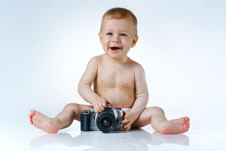 Eight month baby trying to be photographer and playing with camera on white background with reflectionの写真素材