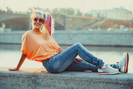 Young teenage style woman sitting on stone quay at morning sunrise.